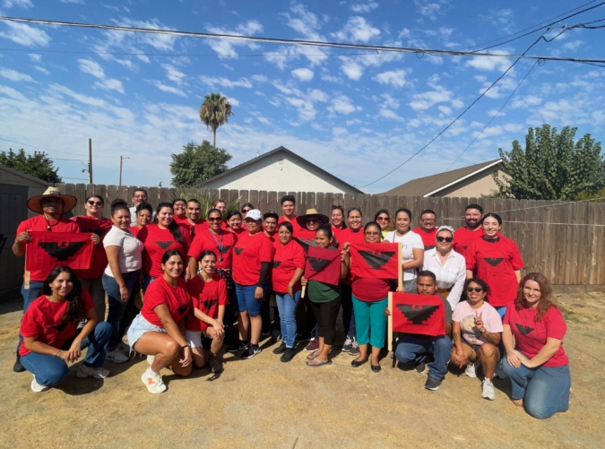 SOTU-Farmworkers-photo About 30 UFW members and allies pose as a group in Bakersfield, CA. They wear bright red t-shirts and hold flags with the UFW logo, a stylized black eagle with its wings shaped like an inverted Aztec pyramid.