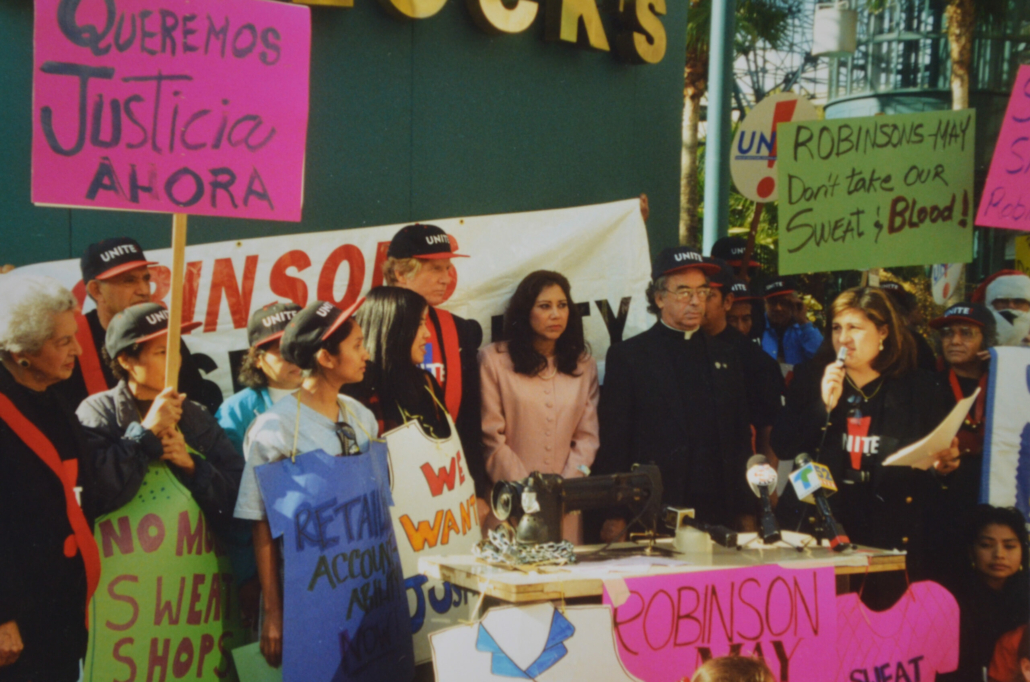 Director Steve Nutter, Assemblymember Hilda Solis, and Father Pedro Villaroya stand with Thai workers from El Monte at UNITE! rally, while organizer Cristina Vásquez speaks at rally outside Robinsons-May in Santa Monica, CA in December 1997. Steve Nutter Collection, IRLE Archives.